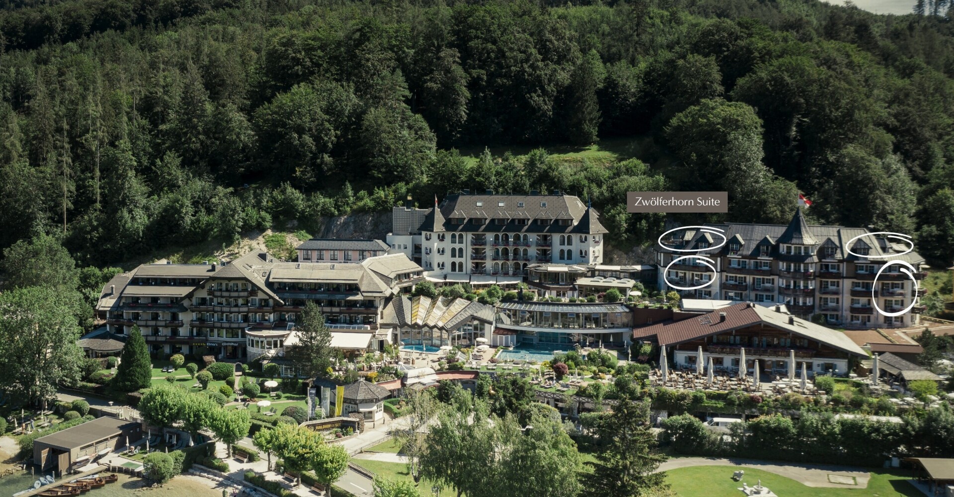 Aerial view of a scenic lakeside hotel surrounded by lush greenery, with labeled "Zwölferhorn Suite."