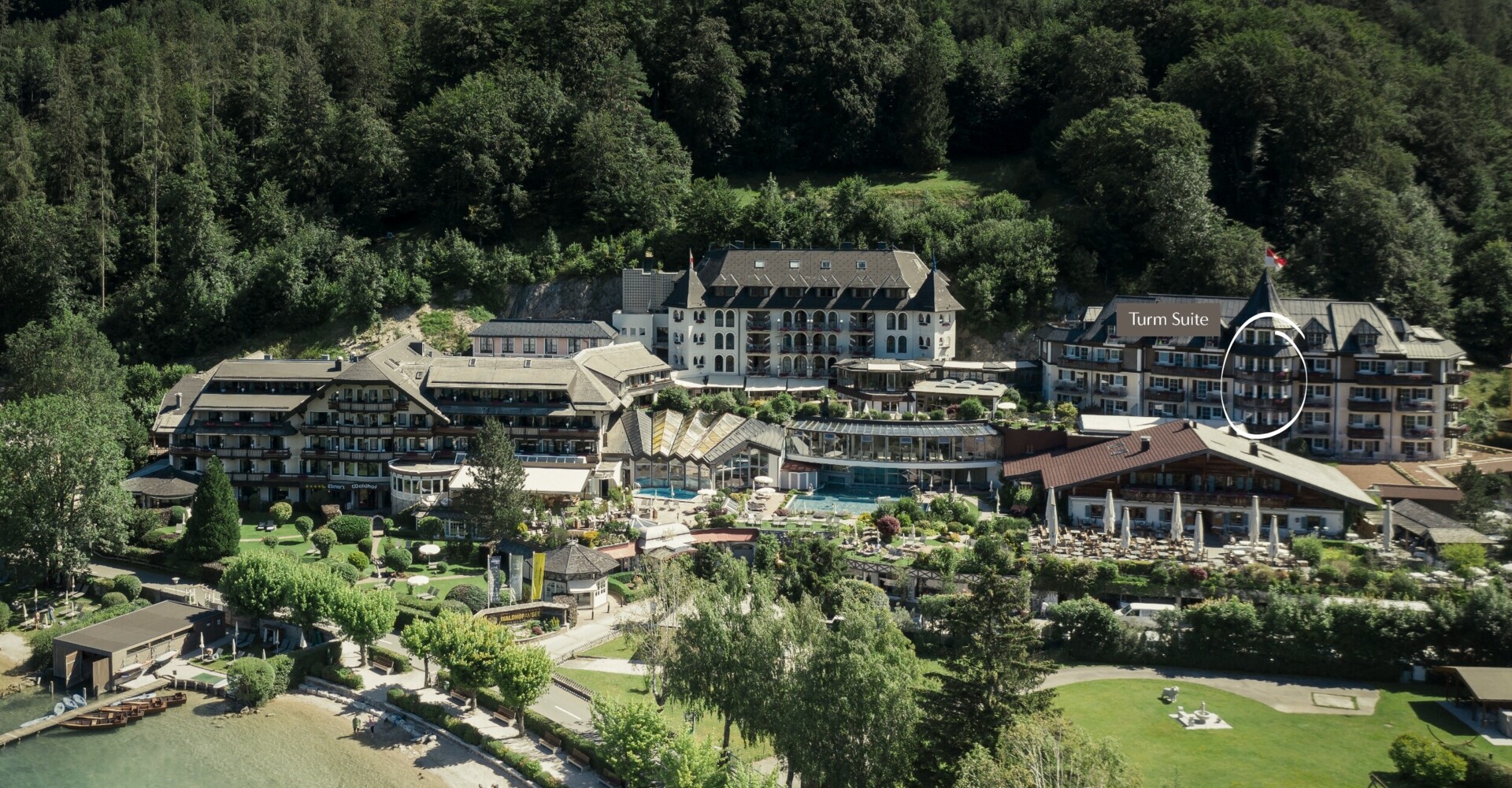 Luftaufnahme des Waldhof Fuschlsee Resorts am Seeufer inmitten von grünen Bäumen, mit markierter Turm Suite auf der rechten Seite.