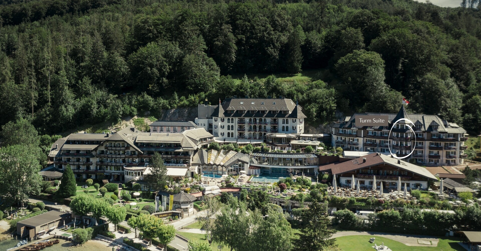 Aerial view of a lush, scenic lakeside hotel surrounded by trees, with a highlighted "Turm Suite" section.