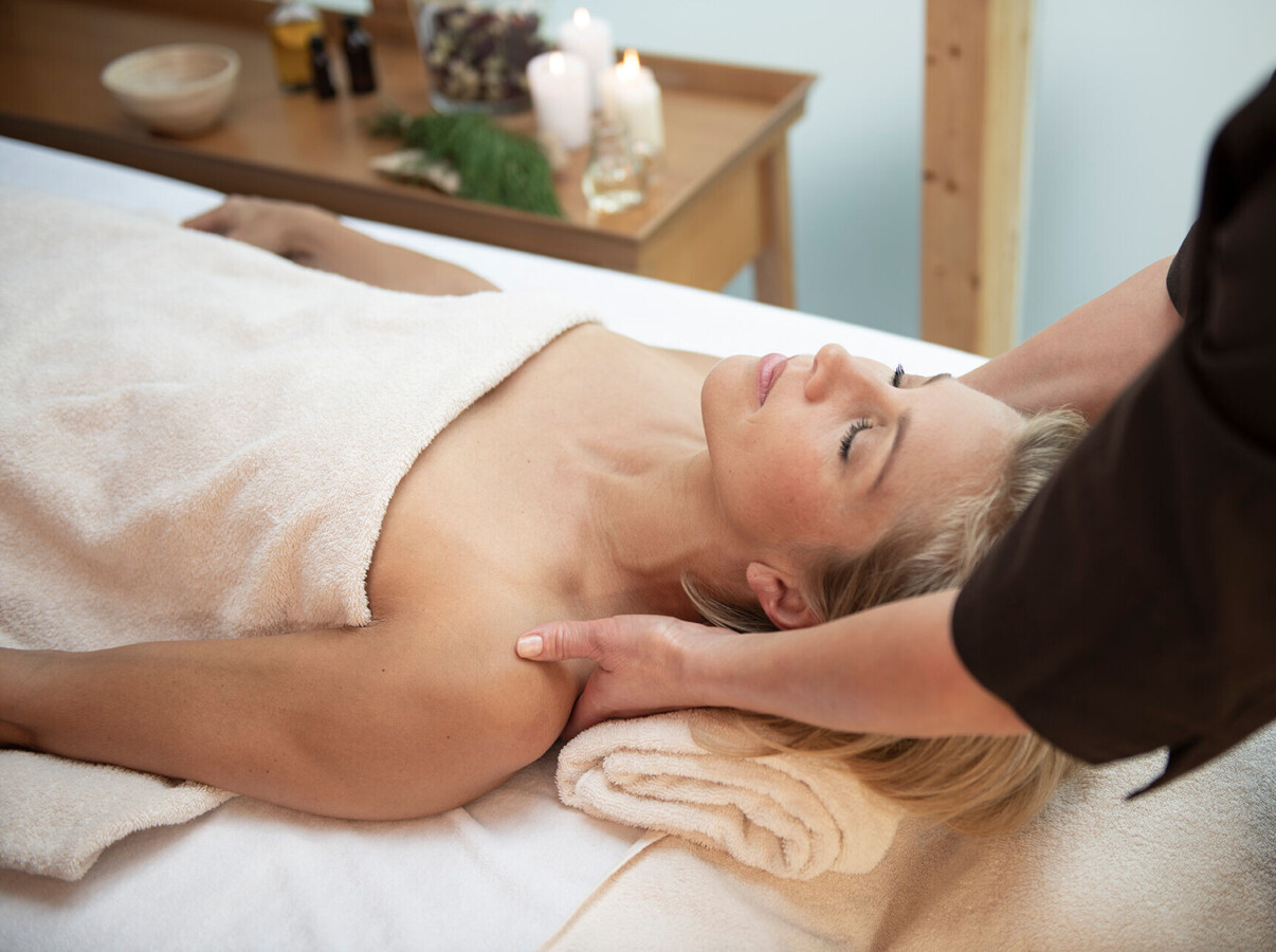 A person receiving a relaxing massage with candles and oils in the background, promoting wellness and tranquility.