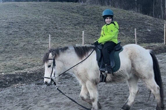 Ein Kind reitet ein Pony in einer ländlichen Umgebung, umgeben von Bäumen.
