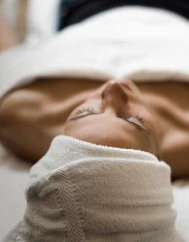 Person relaxing with a towel on their head, lying on a spa bed.