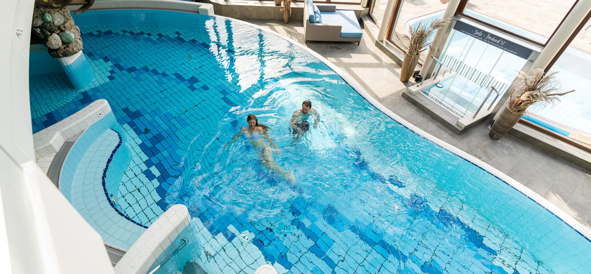 Ein Pärchen schimmt im Indoor-Pool im Wellnessbereich im Wellnesshotel Ebner's Waldhof im Salzkammergut.