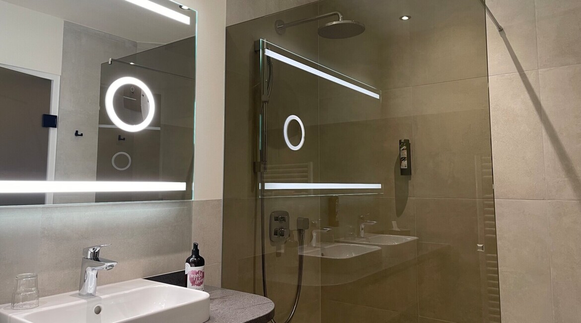 Modern bathroom with illuminated mirror, glass shower, and sleek sink.
