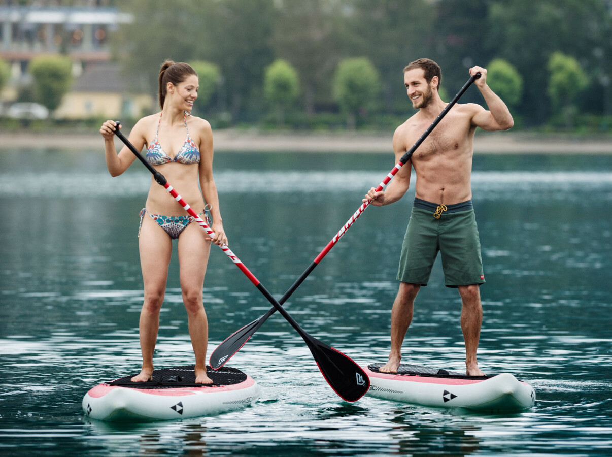 Two people paddleboarding on a calm lake, surrounded by lush greenery.