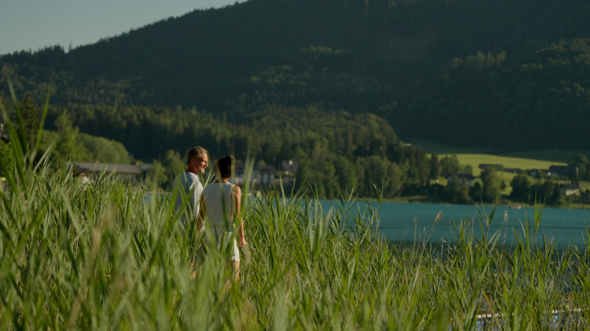 Two people enjoying a lush, scenic view of a lake surrounded by greenery and hills.