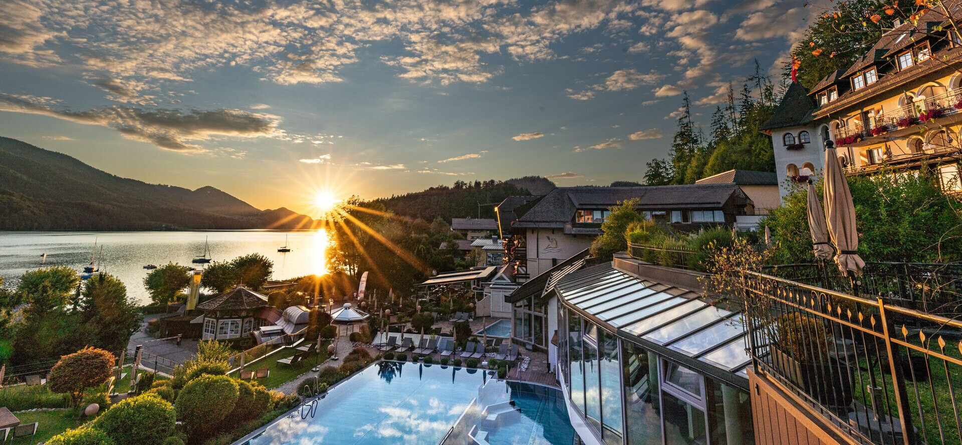 Sonnenuntergang über dem Fuschlsee im Sommer mit Blick auf den Wellnessbereich des Hotel Ebner's Waldhof am See.