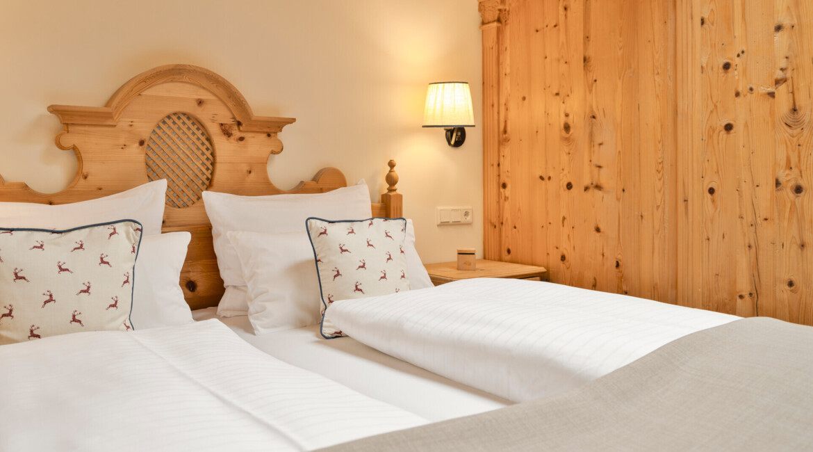 Doppelbett mit Holzverkleidung und Kissen mit Hirschmuster in einem stilvollen Hotelzimmer.