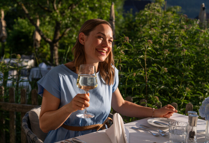 Kulinarik genießen im Urlaub für Alleinreisende - Junge Dame mit Weinglas auf der Terrasse beim Abendessen.