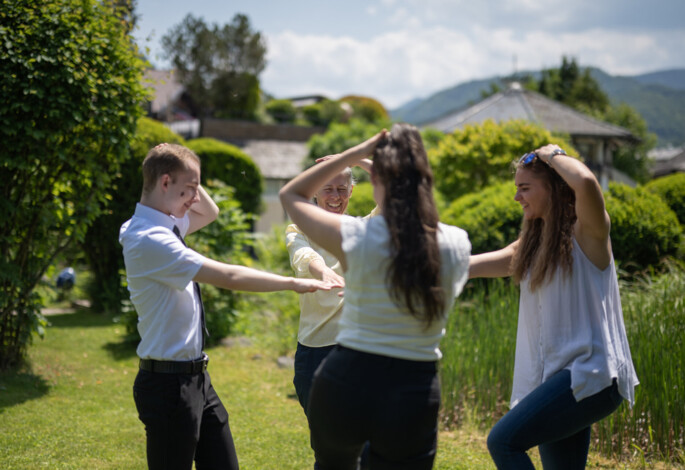 Eine Gruppe von Menschen tanzt fröhlich im Garten bei sonnigem Wetter.