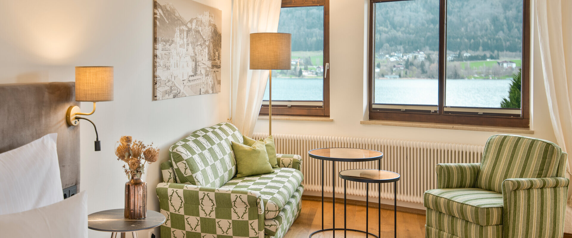Bright room with patterned furniture, large windows showcasing a lake and mountain view, and a cozy ambiance.