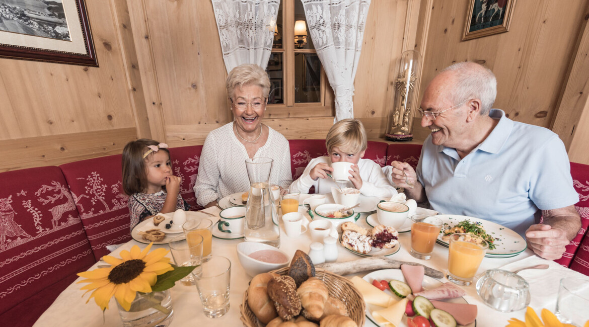 Familie genießt ein Frühstück in gemütlichem, alpinem Ambiente mit Holzvertäfelung und reich gedecktem Tisch.