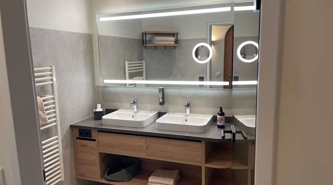 Modern bathroom with double sinks, large mirror, and wooden cabinetry.