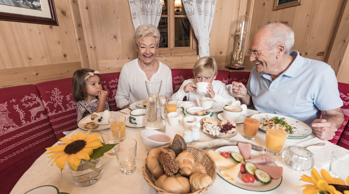 Family enjoying breakfast in a cozy wooden room, with a table set with various dishes and drinks.