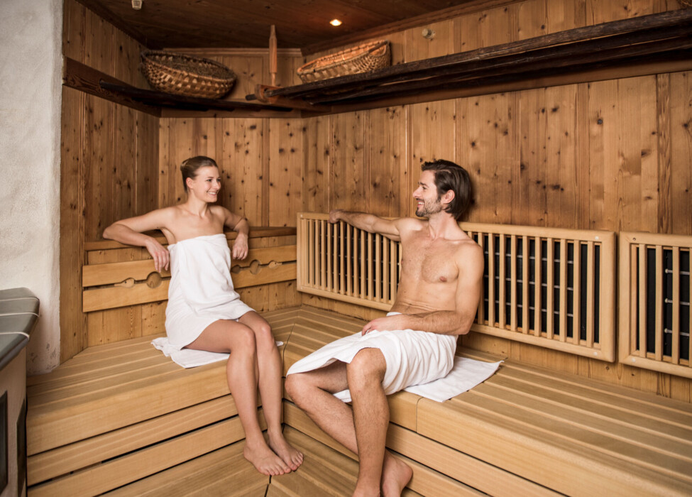 Two people relaxing in a wooden sauna, wrapped in towels, enjoying a serene atmosphere.
