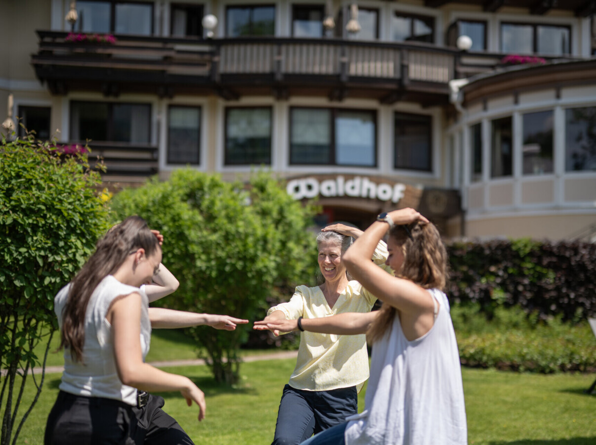 Personen tanzen fröhlich im Garten vor einem Gebäude mit dem Schild "Waldhof".
