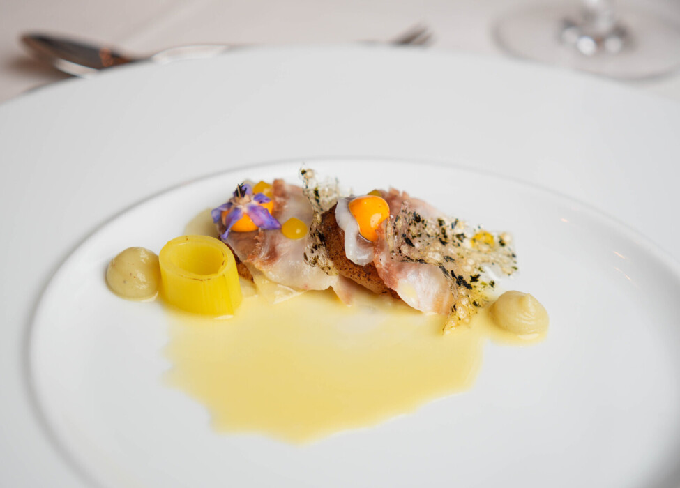 Elegant gourmet dish with delicate garnishes and a vibrant sauce on a white plate.