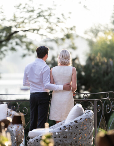 A couple stands on a terrace overlooking a serene landscape with elegant seating, enjoying a peaceful moment together.