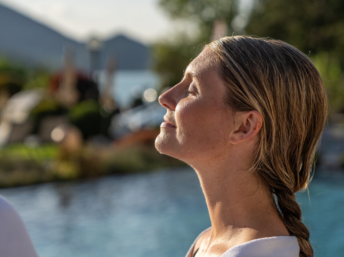 Dame entspannt in der wärmende Sonne am Pool im Hotel Ebner's Waldhof am See.