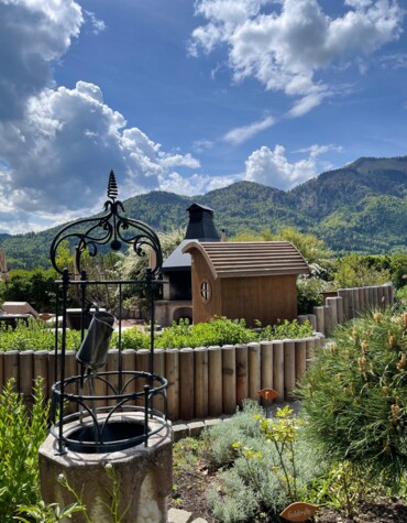 Ein Brunnen im Garten mit Bergen im Hintergrund unter einem bewölkten Himmel.