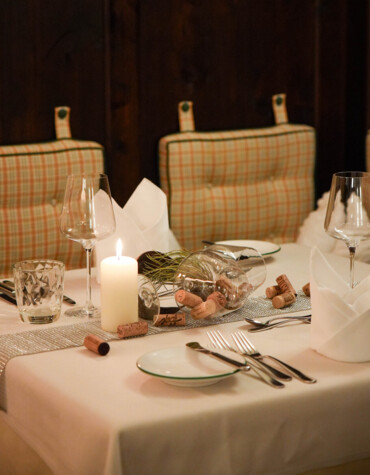 Elegant dining table set with glassware, a lit candle, and wine corks on a white tablecloth, creating a cozy ambiance.