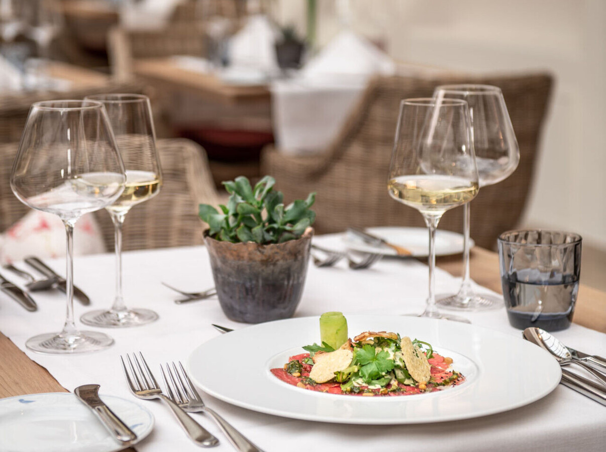 Elegant restaurant table setting with a gourmet dish, wine glasses, and a small plant, creating a cozy and inviting dining atmosphere.