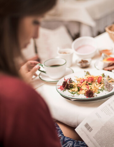 A person enjoys breakfast while reading a newspaper at Waldhof Fuschlsee Resort, featuring a variety of dishes, coffee, and a glass of juice.
