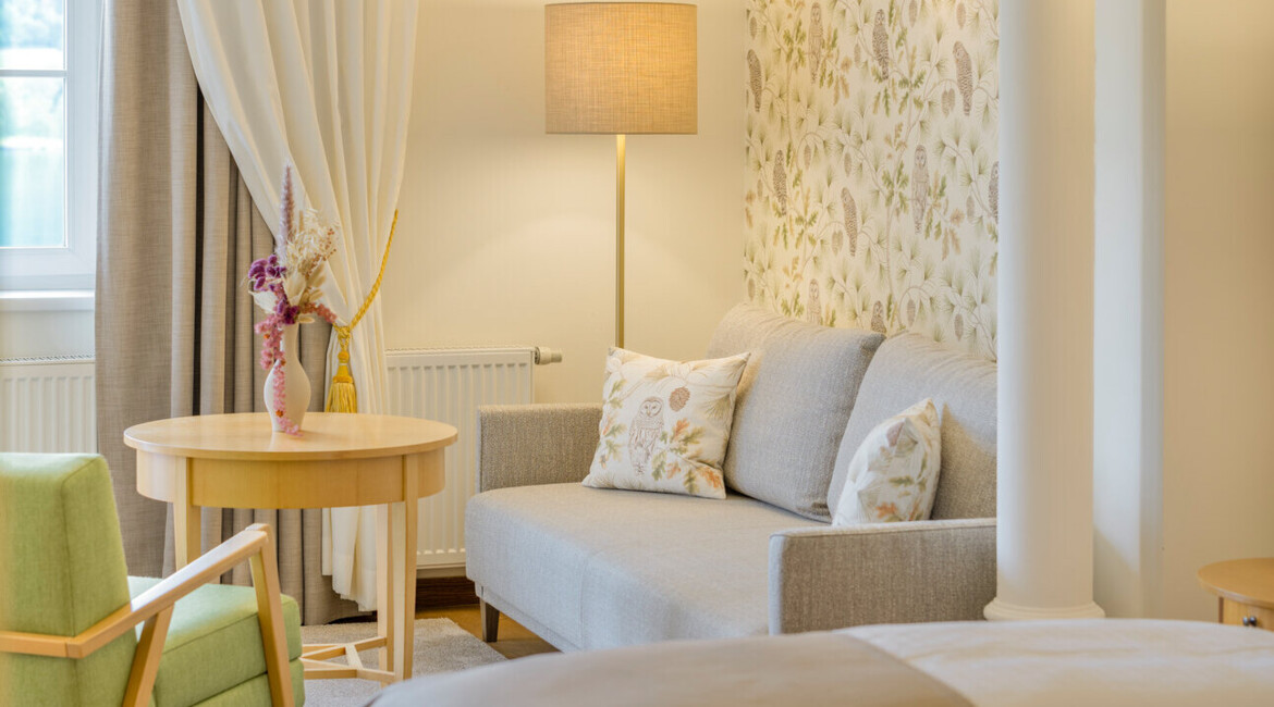 Helles Hotelzimmer mit elegantem Design, gemütlichem Sofa, stilvoller Beleuchtung und floralem Tapetenmuster.