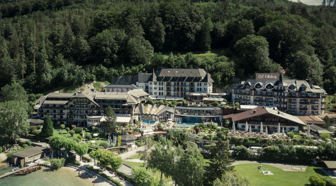 Aerial view of a scenic hotel surrounded by lush greenery near a lake.