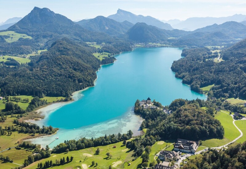 Aerial view of a vibrant turquoise lake surrounded by lush greenery and mountains, showcasing a scenic landscape.