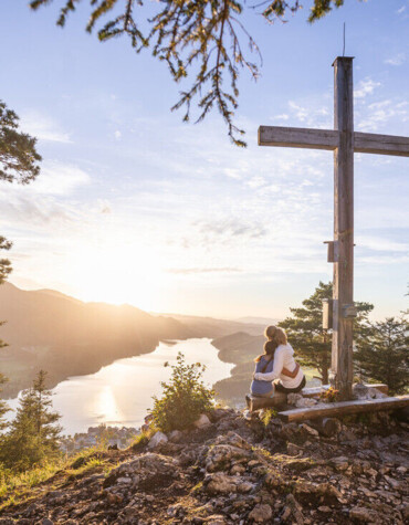 Pärchen vor einem Gipfelkreuz mit Blick auf en Fuschlsee.