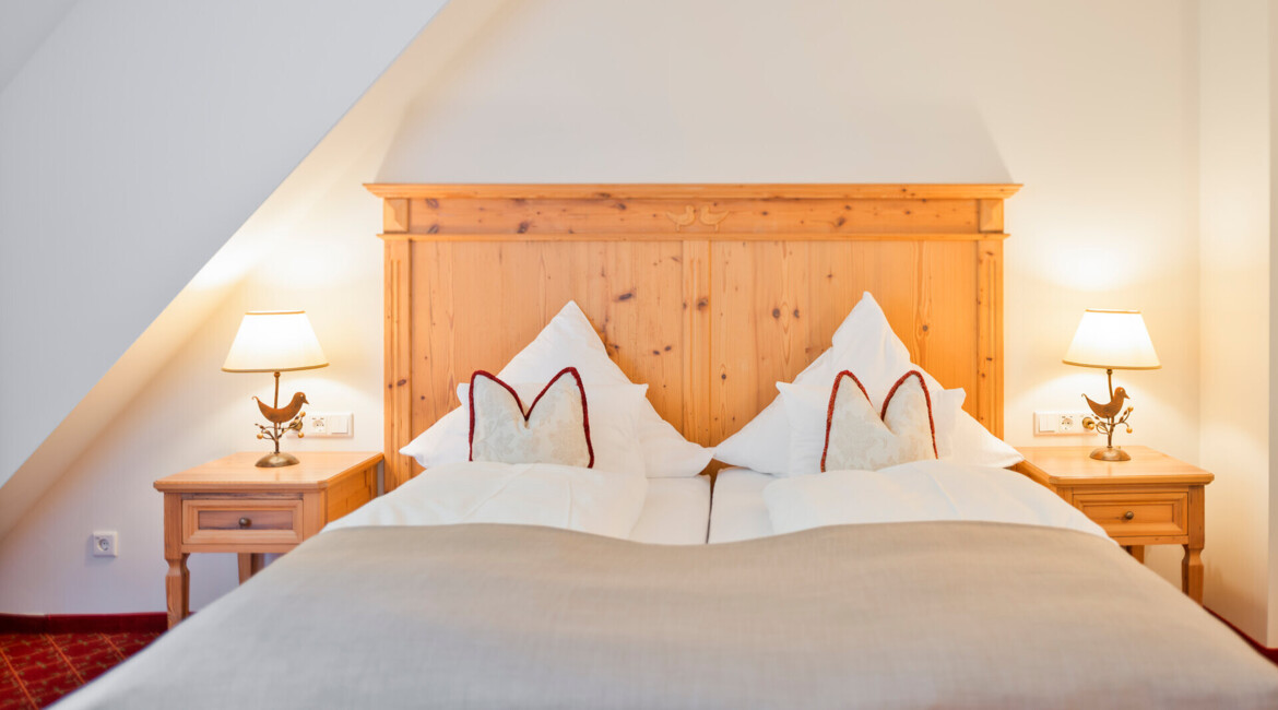 Hotel room at Waldhof Fuschlsee Resort with a wooden headboard, two lamps on nightstands, and neatly arranged pillows on a double bed.