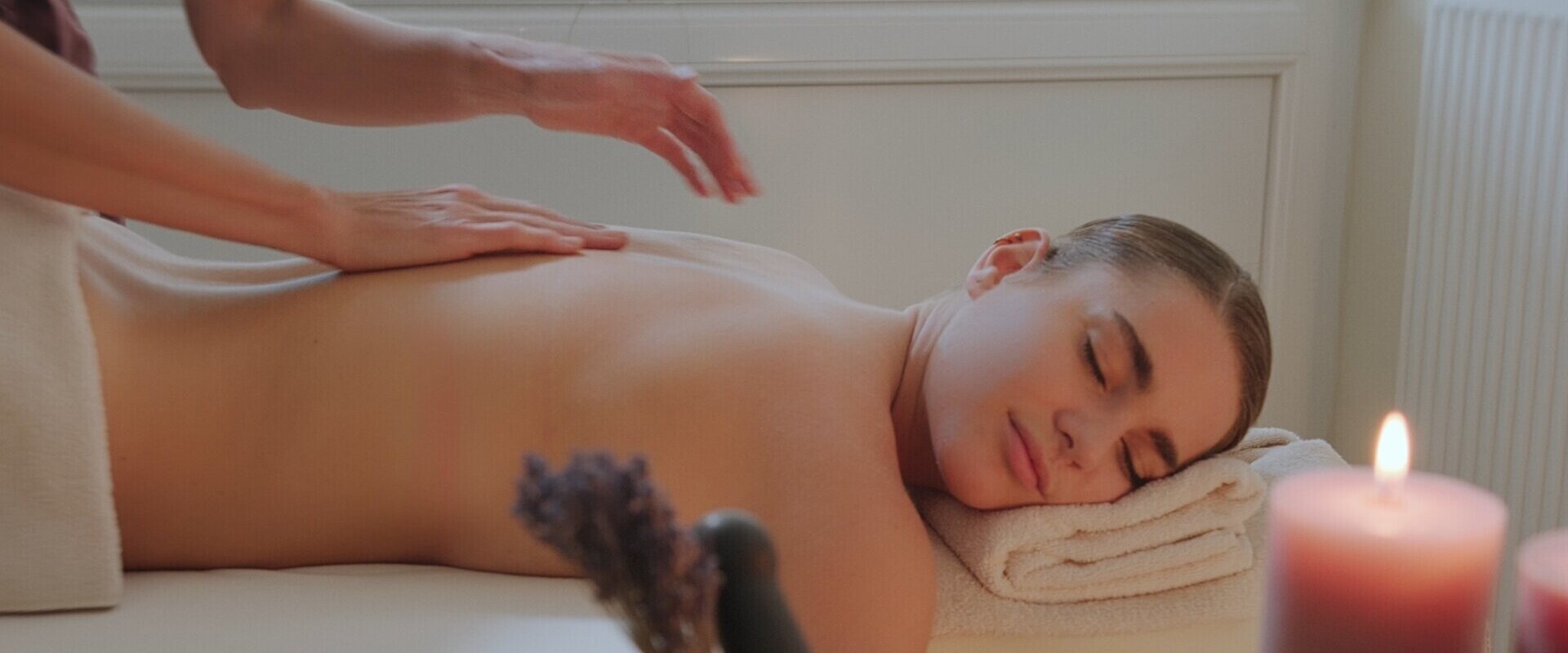 Eine Person genießt eine entspannende Massage in einem Wellnessbereich mit Kerzenlicht.