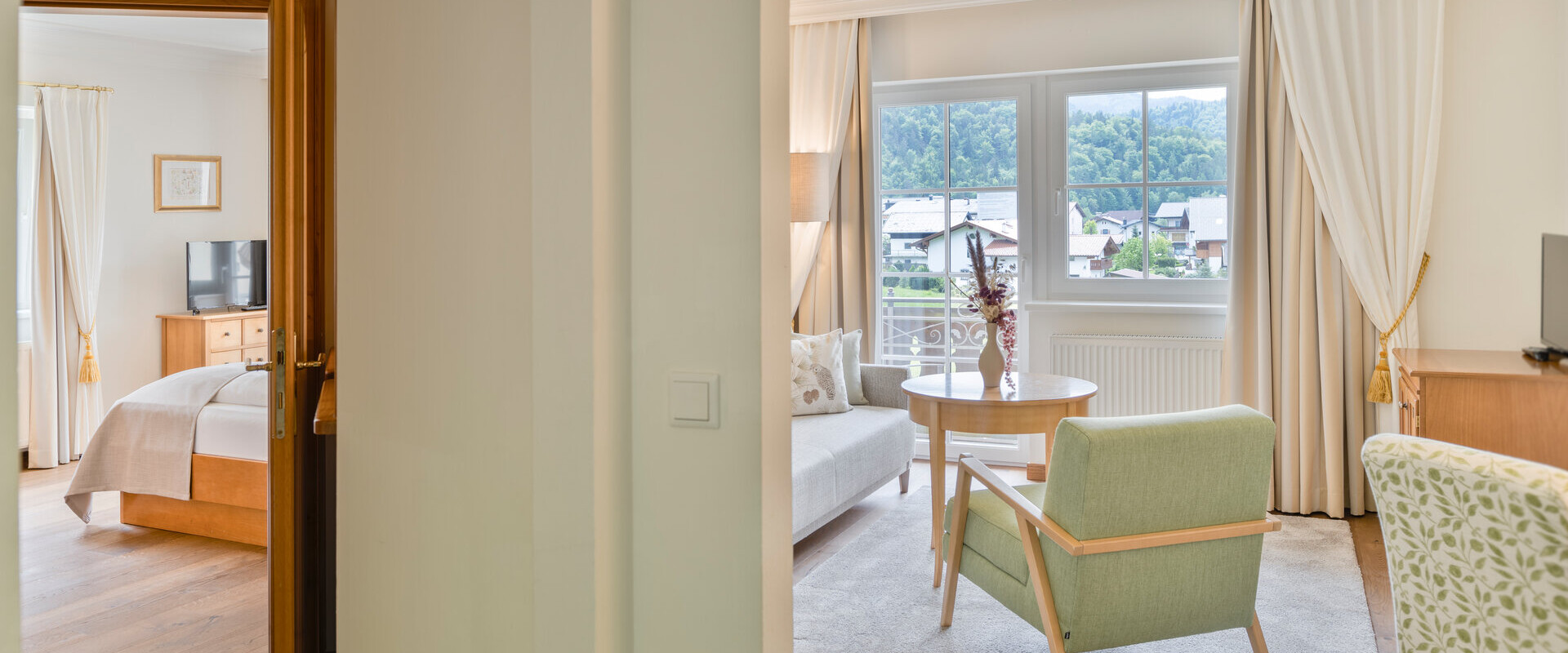 A cozy hotel suite with a bedroom and a living area, featuring elegant furnishings and a scenic view through large windows.