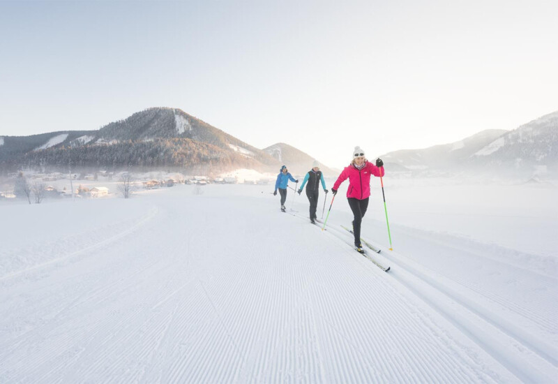 People cross-country skiing on a snow-covered trail with mountains in the background.