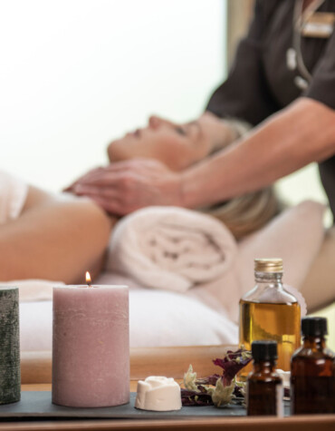 A woman enjoys a relaxing massage with candles and essential oils nearby, creating a tranquil spa atmosphere.