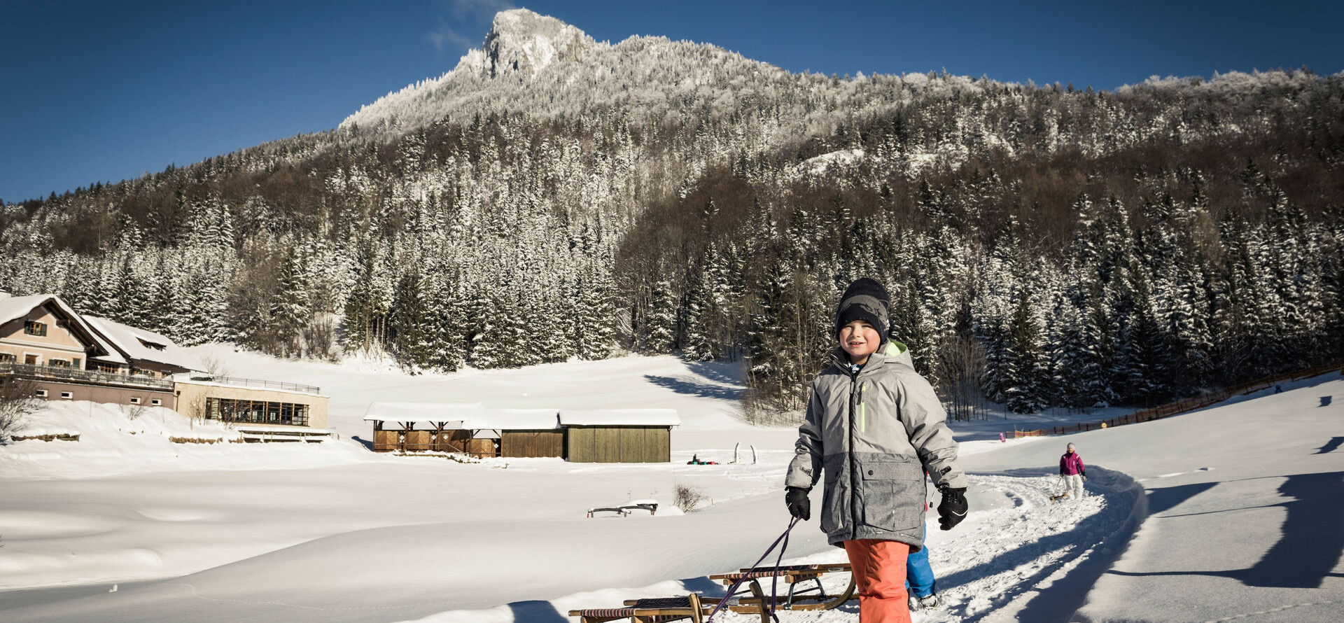 Kinder mit Schlitten beim Spielen im Tiefschnee auf der Waldhofalm am Fuschlsee.