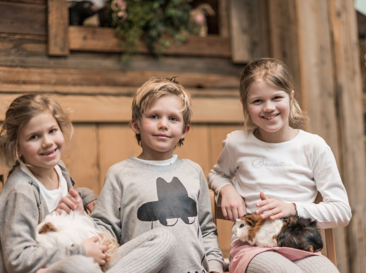 Children smiling and holding guinea pigs in a cozy wooden setting.