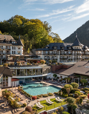 Luxurious hotel nestled in lush greenery, featuring a scenic outdoor pool and elegant architecture, surrounded by forested hills.