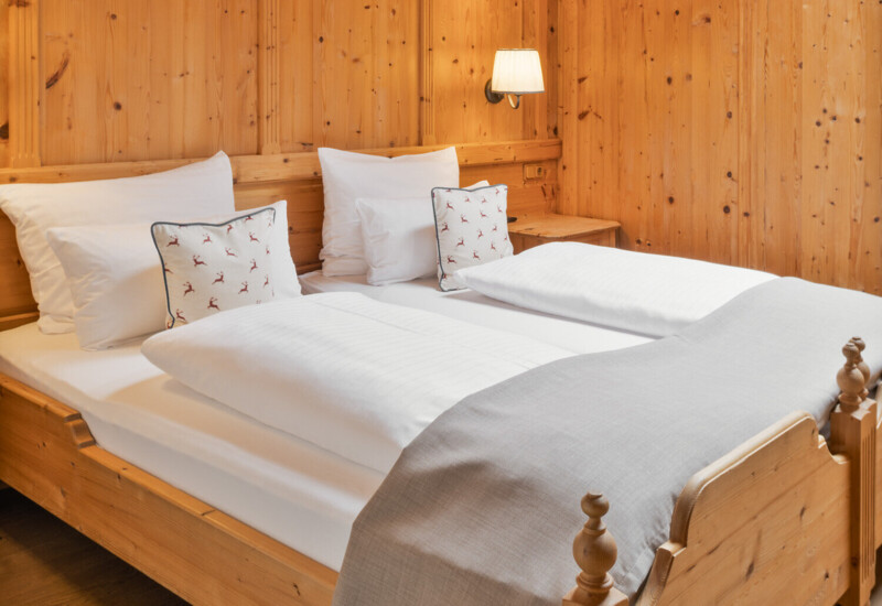 Hotelzimmer mit Holzverkleidung, Doppelbett mit weißen Kissen und Decken, weiches Licht von der Wandlampe.