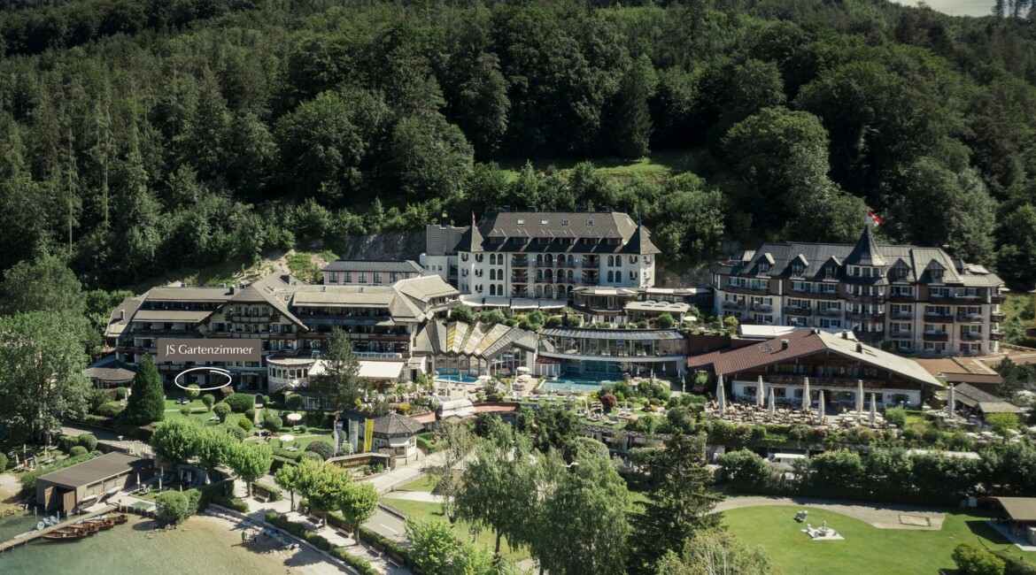 Aerial view of a scenic hotel surrounded by lush greenery near a lakeside.