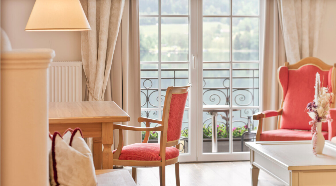 Elegant hotel room with red chairs, wooden table, and large windows offering a scenic view.