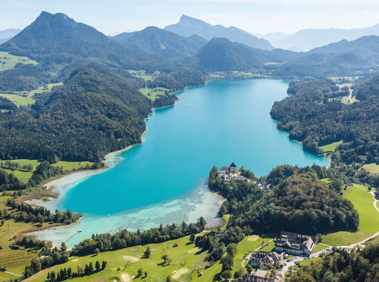 Aerial view of a vibrant turquoise lake surrounded by lush greenery and mountains, showcasing a scenic landscape.