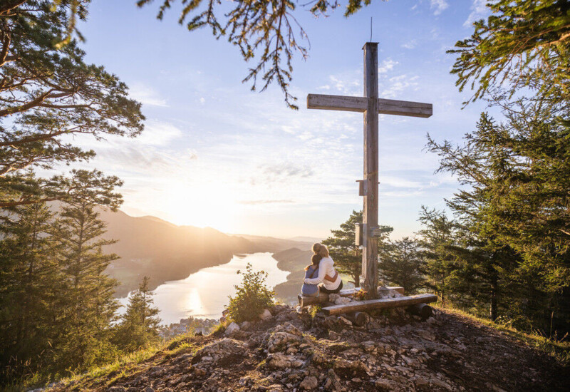 Pärchen vor einem Gipfelkreuz mit Blick auf en Fuschlsee.