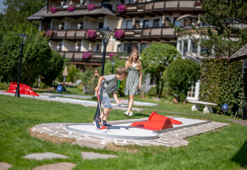 Kinder spielen auf dem hoteleigenen Minigolf-Platz im Familienhotel Ebner's Waldhof am Fuschlsee.