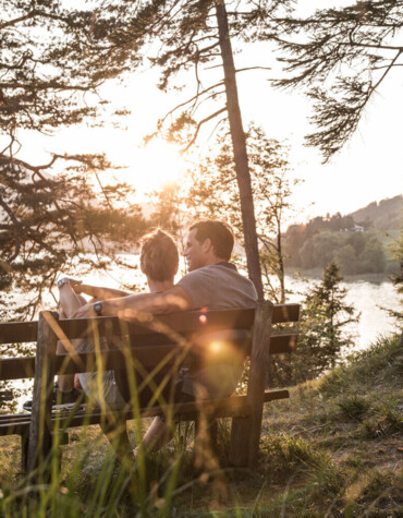 Ein Paar sitzt auf einer Bank im Wald und genießt den Sonnenuntergang am Fuschlsee.